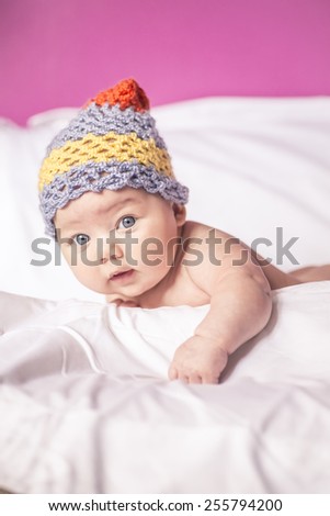 little girl lying on her stomach on the bed, blue eyes, and fun to knit cap on his head, american baby