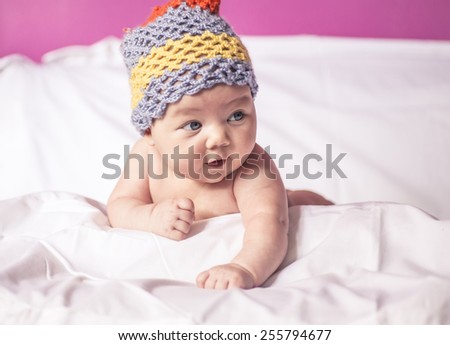 little girl lying on her stomach on the bed, blue eyes, and fun to knit cap on his hea, baby
