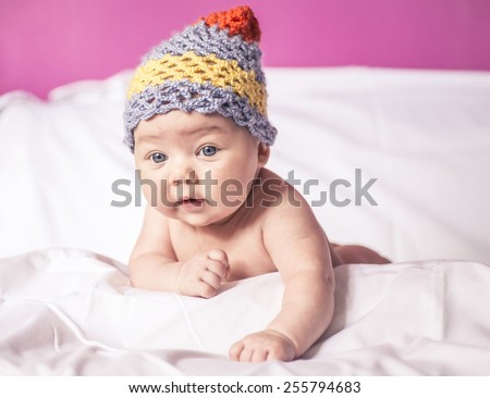 little girl lying on her stomach on the bed, big blue eyes, and fun to knit cap on his head.