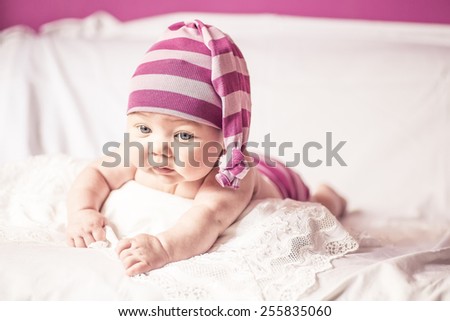funny little girl lying on the bed and looking to the side, striped purple stocking on his head, like a gnome