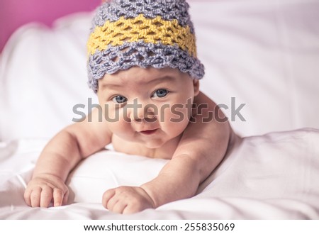 little girl lying on her stomach on the bed, blue eyes, and fun to knit cap on his head.