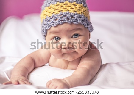 little girl lying on her stomach on the bed, blue eyes, and fun to knit cap on his head, fan photo