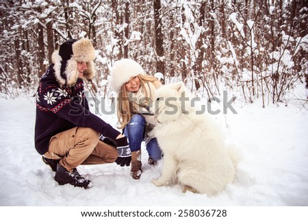 the guy sitting next to a girl, the girl petting a white dog, the guy looks up and smiles, winter in the woods.