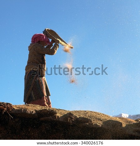 WESTERN NEPAL, 15th NOVEMBER 2013 - Nepalese woman cleaning corn in wind on roof of building. Typical woman work in Nepal