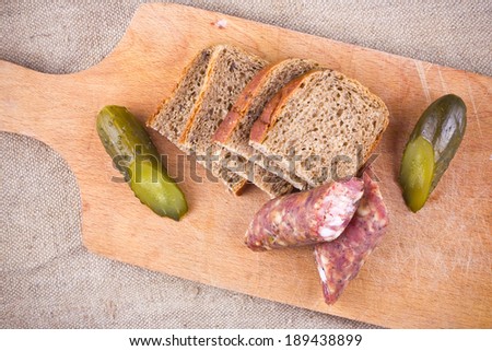 Polish food - bread, cucumber and sausage. Wooden board on linen fabric.