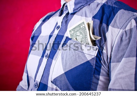 Man dressed in blue shirt holding dollars in his pocket.