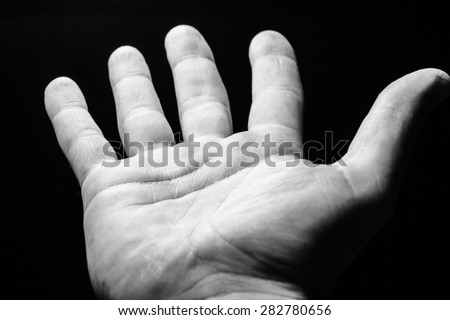 Hand begging for help on black background.