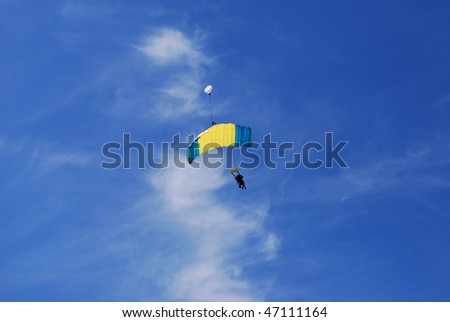 skydiver floating to land with parachute in a beautiful blue sky with small clouds