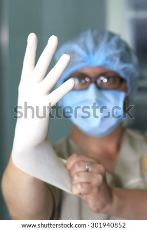 surgeon wears rubber glove in foreground with blurred face on background