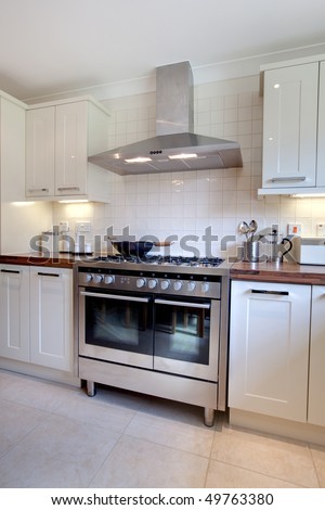 Modern kitchen containing range style stainless steel cooker, matching extractor hood, cupboards and array of utensils and jars standin on the worktop