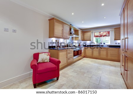 Modern fitted kitchen interior with built in appliances, granite worktops, tiled floor and red armchair