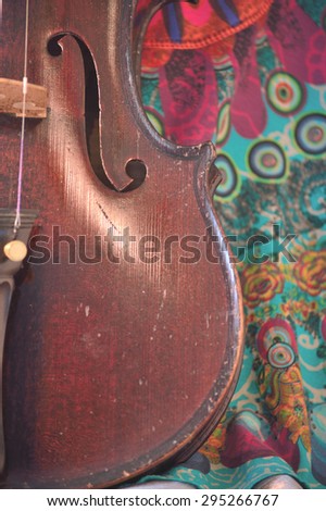 Closeup of a violin against a bright, artsy fabric background. Violin is an antique from the early 1800\'s in a dark stain (original finish). Vertical orientation.