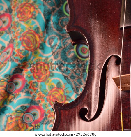 Extreme closeup of violin side against a happy, colorful printed fabric.Violin is an antique from the early 1800\'s in a dark stain (original finish). Square composition.