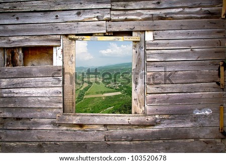 View from the old window - wooden frame of rural landscape. Window on the wooden wall with a farmland view. Countryside with green fields - view through the window on the wooden background.