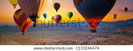 Many colorful hot air balloons flight above mountains - panorama of Cappadocia at sunrise. Wide landscape of Goreme valley in Cappadocia -  billboard background for your travel concept in Turkey.