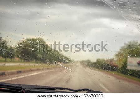 Driving Car In The Rain On Wet Road. Rainy Weather Through The Car Window. Rain Through Wind-Screen Of Moving Car. View Through The Car Window In The Rain. Car Windshield Wipers On In The Rain.