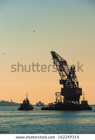 Industrial landscape - sea port at sunset. Construction works in the sea at the offshore platform. Skyline with silhouette of marine crane platform and barge.