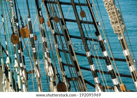 Rigging ropes and pulley at the old ship. Tackles of the ancient sailing vessel. Marine background with wooden rigging and rope ladder. Wooden block, ladder upstairs on the mast. Tackle on the ship.