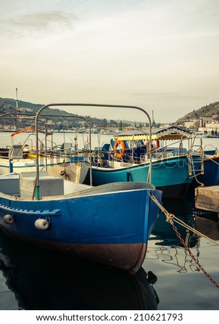 Marine landscape with a boats in harbor. Old boats on pier - fisherman's transport. Bow of the fishing boat with reflection on sea surface. Blue motorboats are moored in harbor.