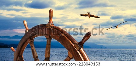Steering wheel at sea background.  Skipper\'s wheel on an old ship. Sea voyage at the seaside with captains wheel of the old vessel, closeup. Marine skyline on the sundown with two seagull on the sky.