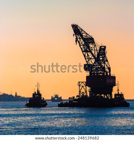 Construction works in the sea at the offshore platform. Skyline with silhouette of marine crane platform and barge. Industrial landscape - sea port at sunset.