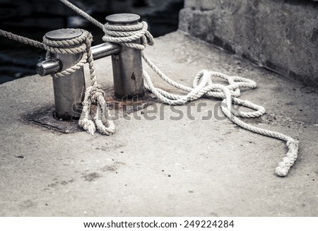 Old bollard with the sea rope. Rope tied in a knot on a bollard in sea harbor. Mooring rope wrapped around the cleat on pier. Mooring equipment - monochrome image.