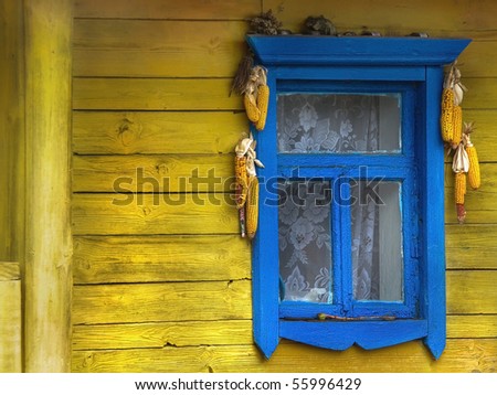 Window on the facade of an old wooden farmhouse. Ukrainian house in the village. Rural window in blue frame with corn cobs at yellow wall.