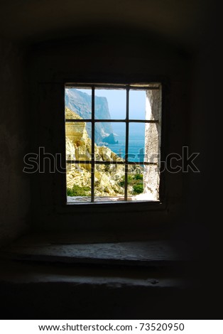 Window lattice in the prison cell. View from the dungeon window -  frame of the see landscape. Ancient prison in historical fortress. Panoramic view inside a barred window on the seascape.