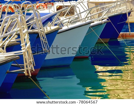 Boats and yachts in the marine harbor. Yachts moored at the pier in the Mediterranean port. White sailboats lined up in a row with the reflections in the water.