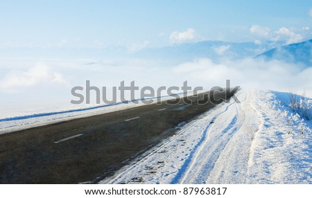 Snow covered road in winter with mountains in the distance. Travel background with mountains and auto track. Snowy highway with cloudy landscape.