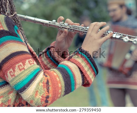 Flute in the girl\'s hands in the foreground with bokeh effect. Funny street musicians playing in the park on the flute and the accordion.