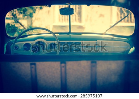 Interior of an old automobile with windshield, steering wheel, dashboard - car into the window frame. Retro car in soft light effect. Vintage photo of family automobile - inside car salon.