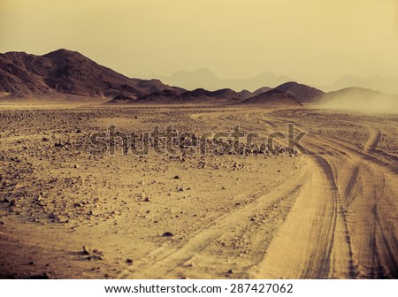 Sahara desert - mountain landscape with dusty offroad and stone hills on a horizon. Exotic adventure or expedition in Arabian desert, extreme travel to Egypt. Sunset in an arid desert.