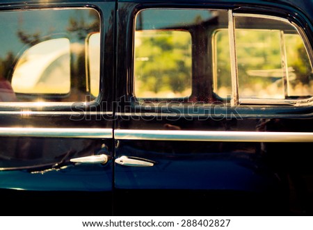Stylish background of the old automobile with door handles and window frames. Retro car in vintage style at sunset light. Oldtimer black automobile, side view.
