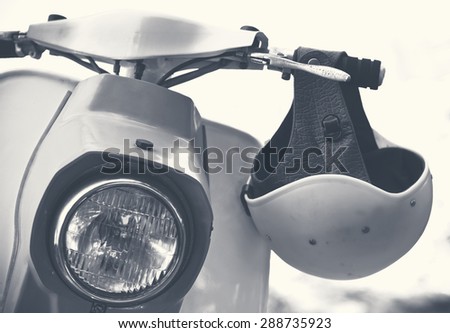 Old scooter with helmet and headlamp closeup. Vintage biker objects - romantic travel on motorbike in retro style. Monochromatic colors on stylish toned photo.