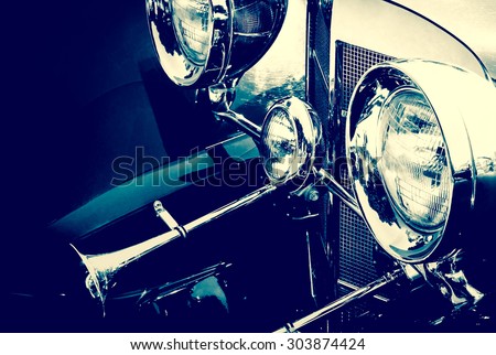 Headlamps of the old automobile. Auto headlights of retro car with chrome parts elements, monochrome vintage photo. Lamps and bumper of the old transport - retro auto closeup.