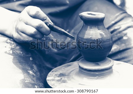 Potter makes on the pottery wheel clay pot. The hands of a potter with the tool, on black and white colors.