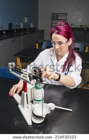 a woman wearing a white coat and safety glasses is doing an experiment in a school laboratory