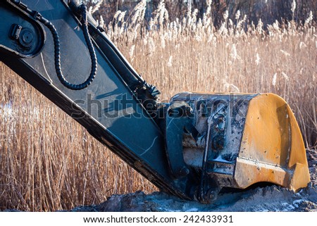 Technology, Transport, Construction. Excavator bucket on a background of dry grass. in frozen ground. Modal sun.