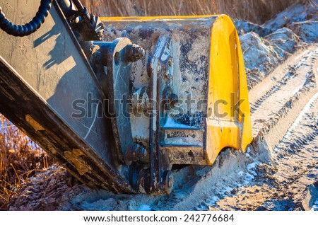 Technology and transport. Close-up of excavator bucket frozen sand and snow. Modal sun, warm light, long shadows.
