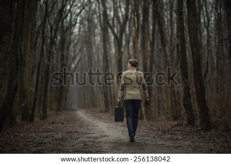 Man in smart casual outfit in the woods with suit case