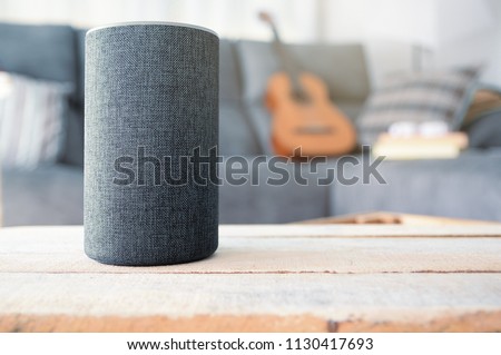 Personal assistant connected loudspeaker on a wooden table in a Smart Home in a living room. Next, a guitar and some books on a sofa. Copy space for Editor\'s text.