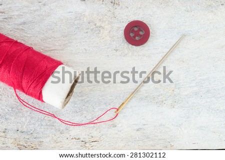 Sewing needle threaded with a red thread ready for sewing. Next , a button. Scene on a white wooden table . Top view.