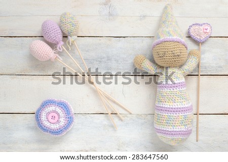 Crochet toy doll with some handmade decoration on a white wooden table. Top view.