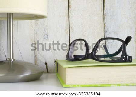 Shelf with glasses on a book and a lamp, ready for reading time. White wooden background. Empty copy space for editor's text.