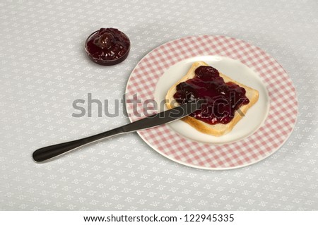 Spread jam on bread with knife. Pink checkered plate