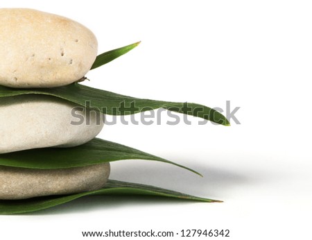 Stacked stones on base of green leafs. White isolated studio shot.
