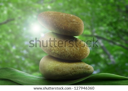 Stacked stones on base of green leafs. Green natural background.