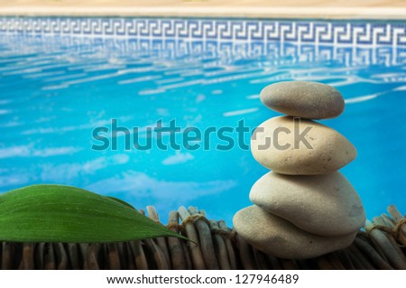 Stacked stones on wooden base for spa and green leaf. Swimming Pool on the background.
