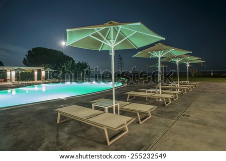 Pool, sunbeds and umbrellas at night. Night lights. Greece, Gythio